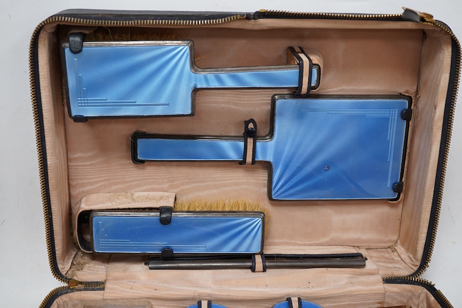 A George V/George VI Art Deco vanity case containing nine silver and blue guilloche enamel mounted items including a hand mirror, brushes, nail implement etc. Walker & Hall, 1936/37, incomplete.